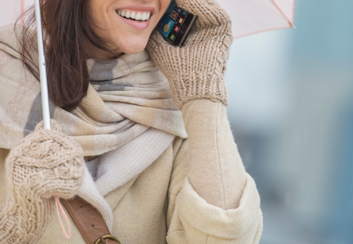 Žena sa kišobranom napolju po zimskom vremenu držu mobilni telefon
