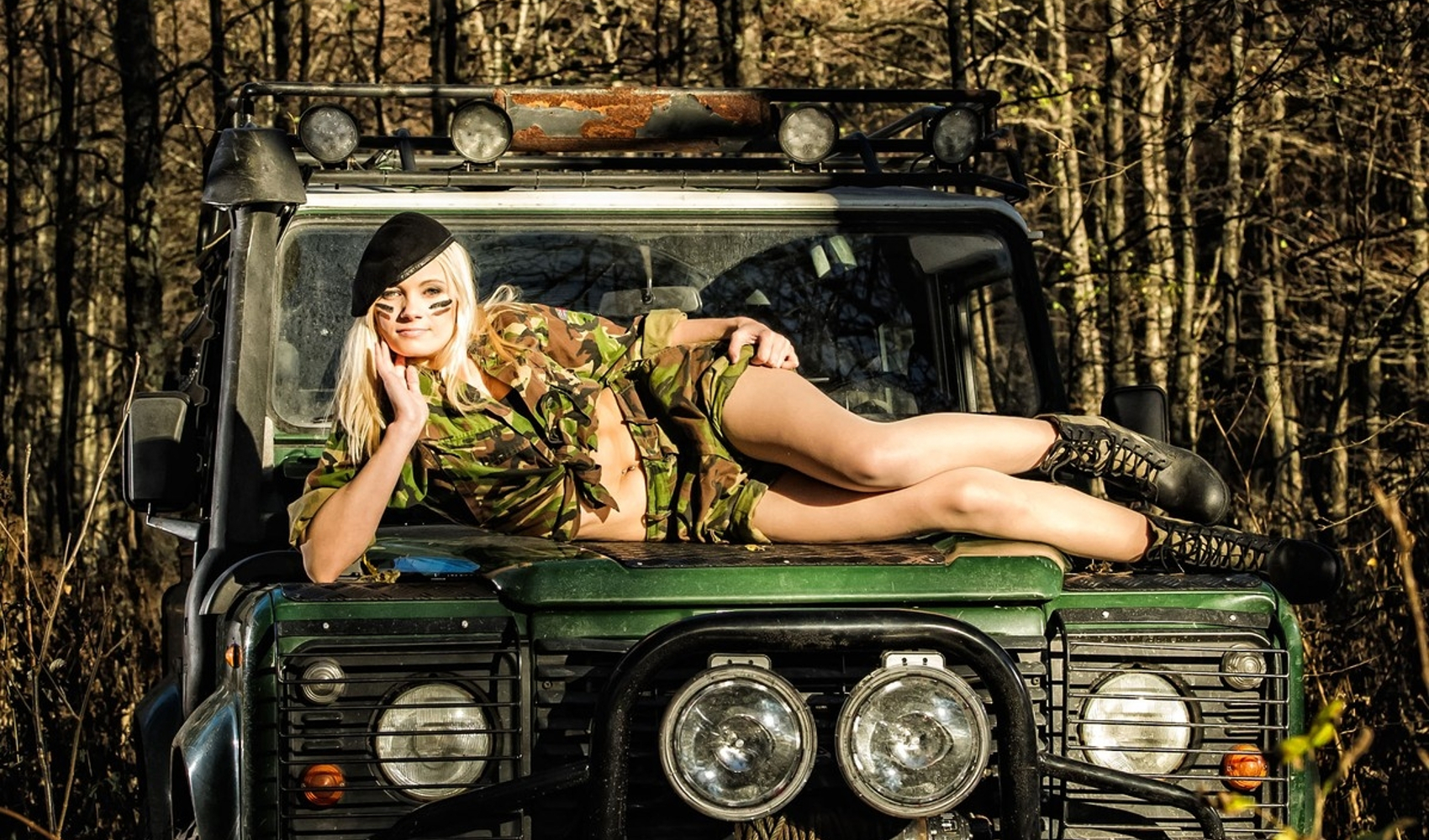 Žena u seksi vojničkoj uniformi leži na vojnom džipu