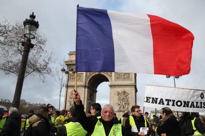 Učesnik protesta u Parizu drži zastavu Francuske ispred Trijumfalne kapije